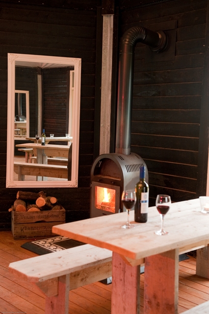 binnenkant Paviljoen met een gestookte kachel en glazen rode wijn op de houten tafel.