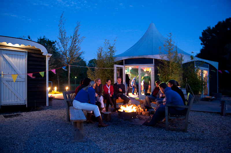 Kampvuur met groep volwassenen eromheen bij de Veldhuysjes.
